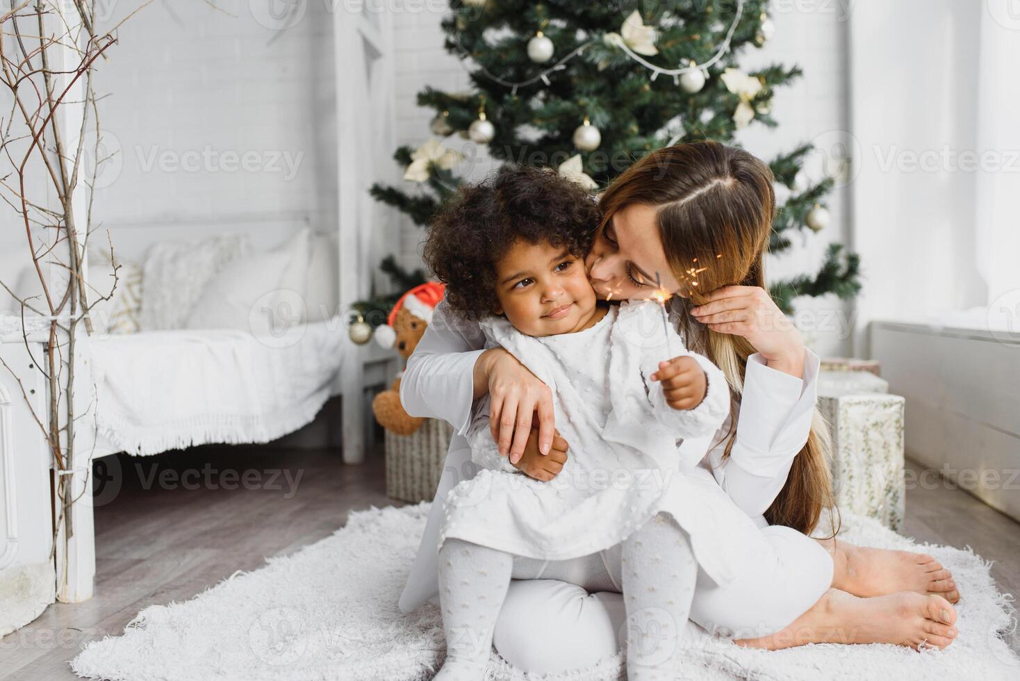 Merry Christmas and Happy Holidays Cheerful mom and her cute daughter at Christmas tree. Parent and little child having fun near Christmas tree indoors. Loving family with presents in room. photo