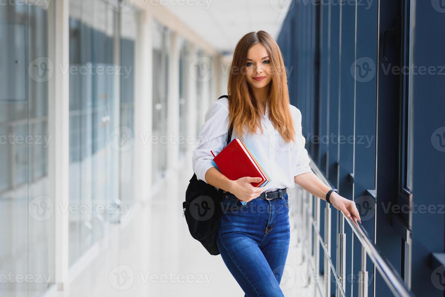 Positivity beautiful girl smiling at camera, standing on corridor with notes as backpack, going to lesson. Happy brunette female student studying in luxury university. photo