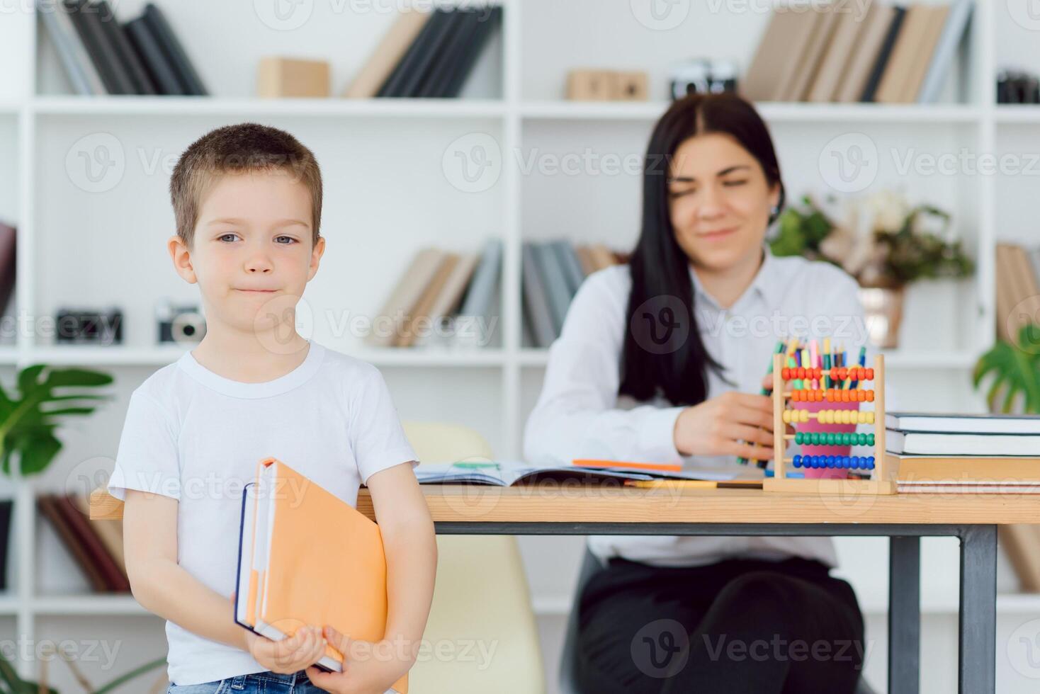 Female private tutor helping young student with homework at desk in bright child's room photo