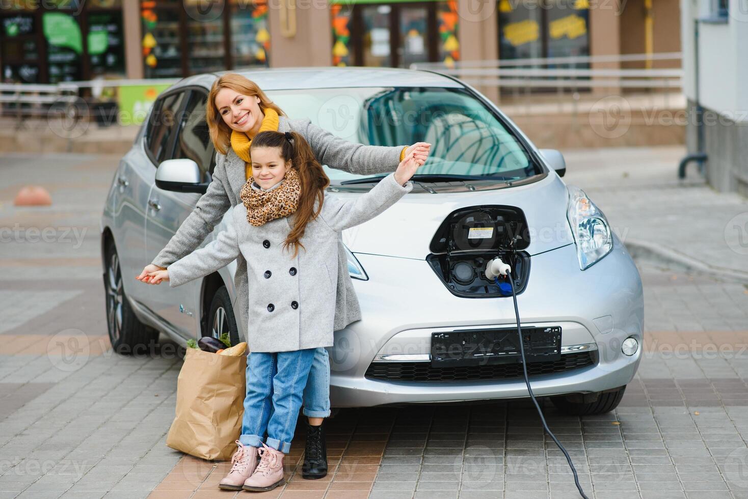 elegante madre y hija cargar un eléctrico auto, y gastar hora juntos. foto