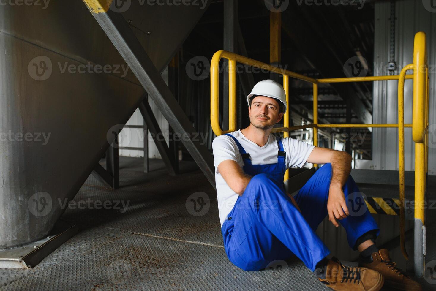 Young smiling professional in overalls and protective helmet standing in front of camera inside large machinebuilding plant photo