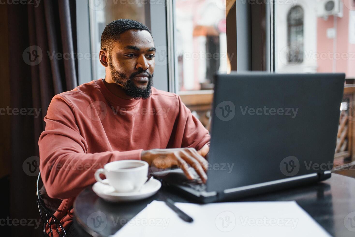 Portrait of happy african businessman sitting in a cafe and working on laptop. photo