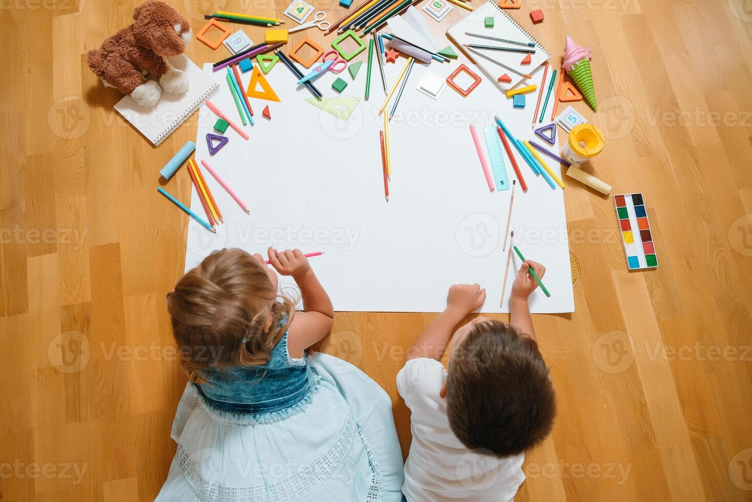 Kids drawing on floor on paper. Preschool boy and girl play on floor with educational toys - blocks, train, railroad, plane. Toys for preschool and kindergarten. Children at home or daycare. Top view. photo