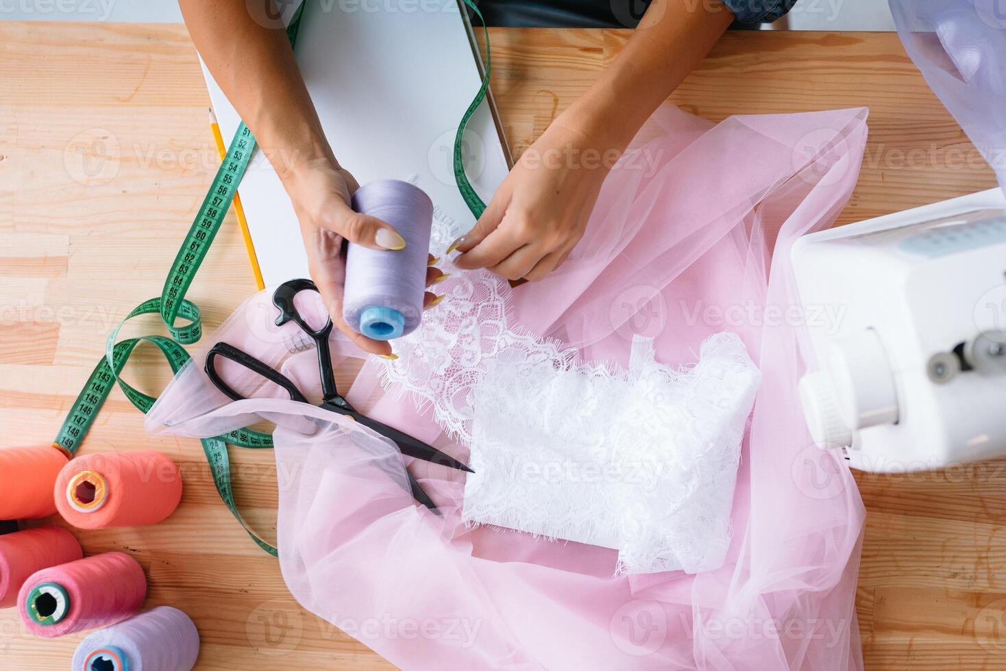 Hands mistress seamstress made a beautiful bright fashionable clothes. The crosslinking parts of the pattern. Work place. Top view. Light Textile industry creative moments. photo