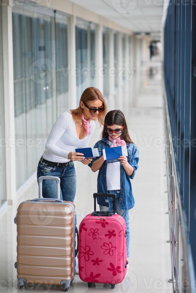 madre y pequeño hija con equipaje y embarque pasar y pasaporte a aeropuerto terminal Listo para vacaciones. alto temporada y vacaciones concepto. relajarse y estilos de vida foto