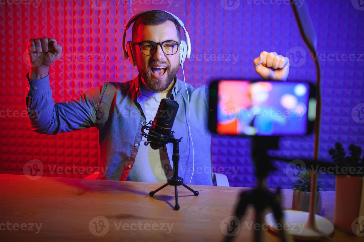 vlogger utilizando teléfono inteligente a película podcast en estudio. blogger con móvil teléfono, micrófono y auriculares rodaje vídeo para social medios de comunicación radiodifusión carrera profesional. foto