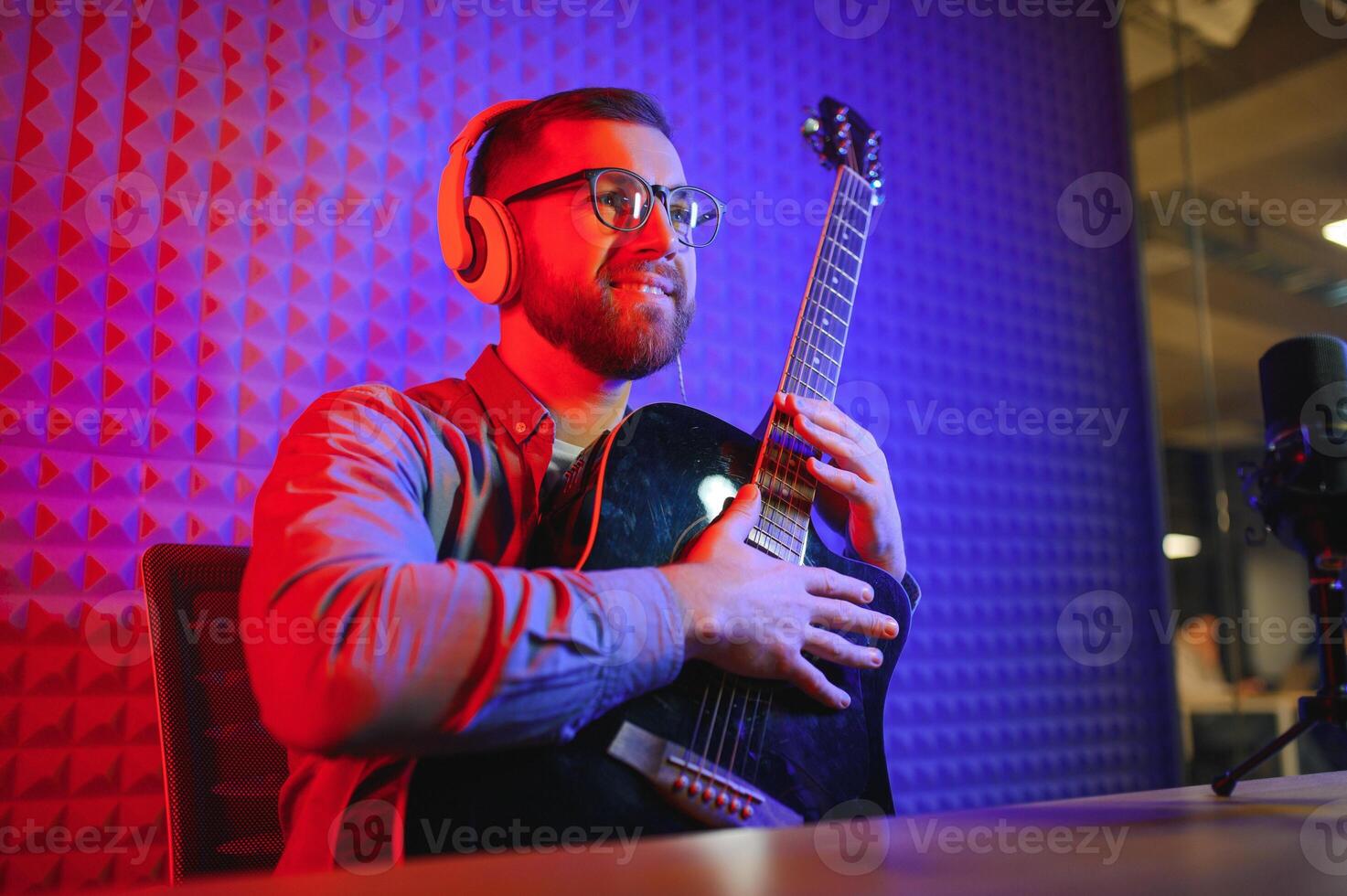 Young Caucasian male singer in headphones hold play guitar record new single on smartphone at home studio. Millennial man artist use musical instrument sing shoot music video on cellphone camera. photo