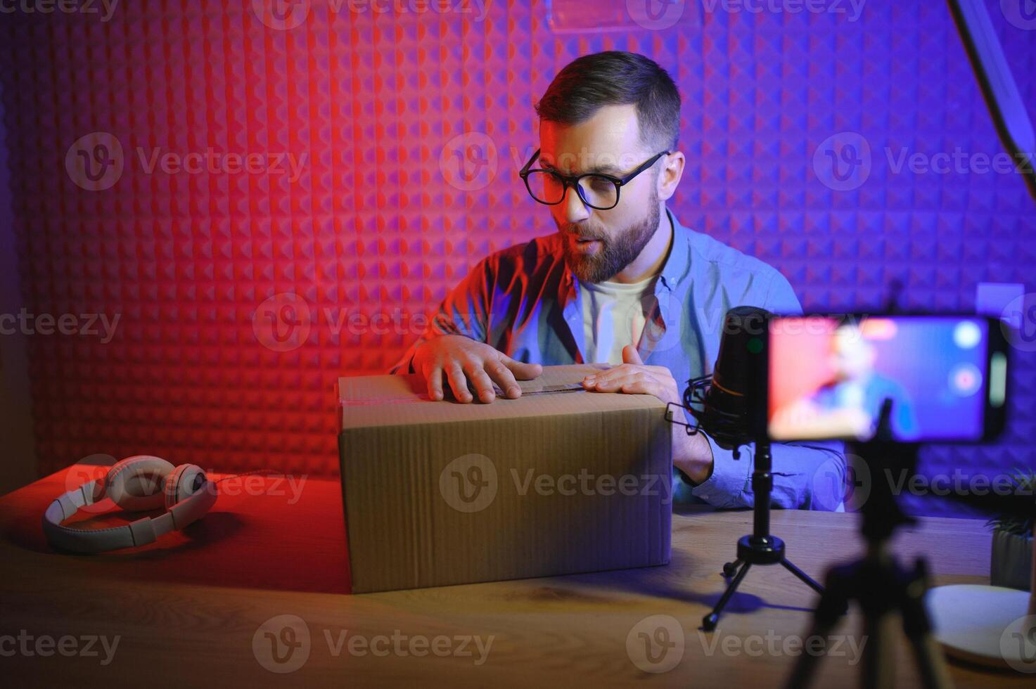 vlogger utilizando teléfono inteligente a película podcast en estudio. blogger con móvil teléfono, micrófono y auriculares rodaje vídeo para social medios de comunicación radiodifusión carrera profesional. foto