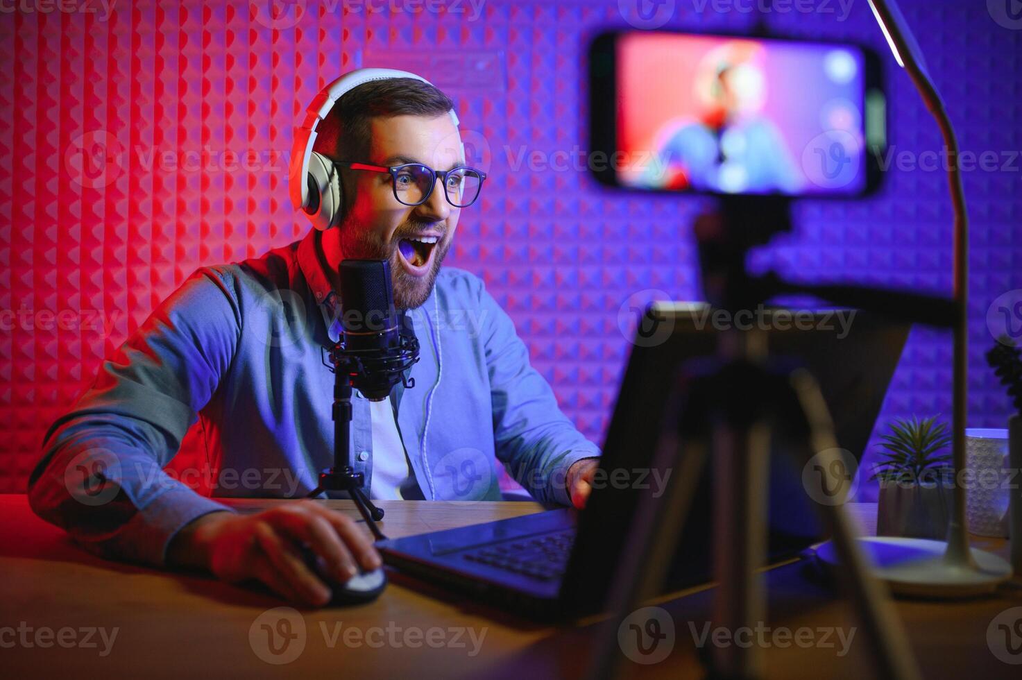 Young man recording or streaming podcast using microphone at his small broadcast studio. Content creator. photo
