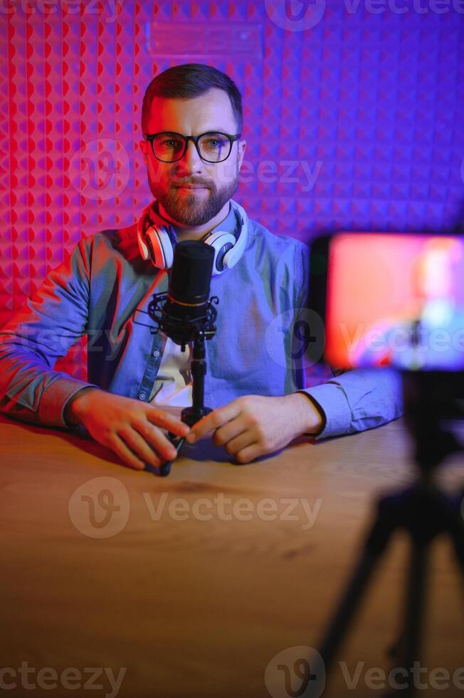 joven hombre grabación o transmisión podcast utilizando micrófono a su pequeño transmitir estudio. contenido creador. foto