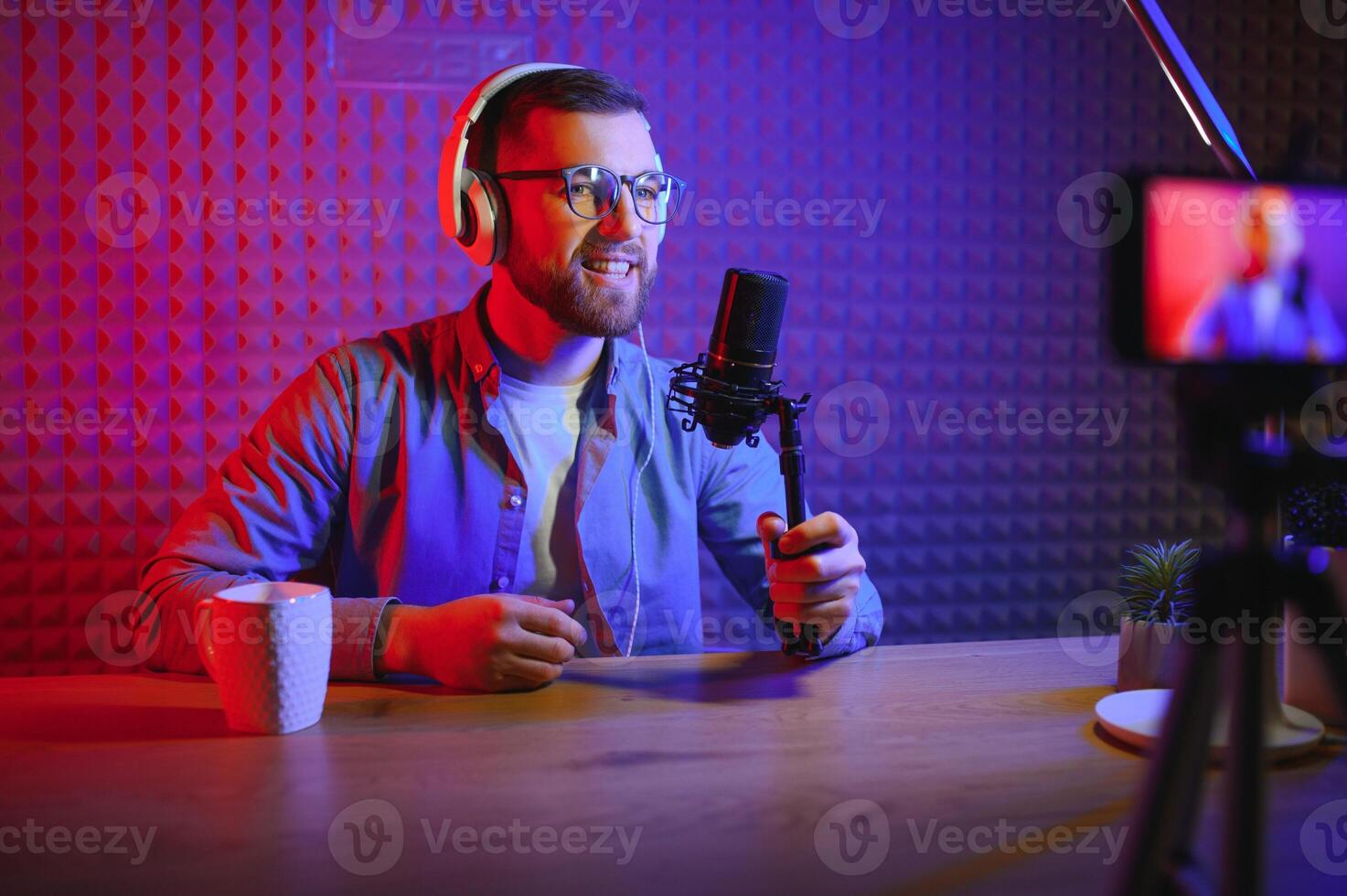 vlogger utilizando teléfono inteligente a película podcast en estudio. blogger con móvil teléfono, micrófono y auriculares rodaje vídeo para social medios de comunicación radiodifusión carrera profesional. foto