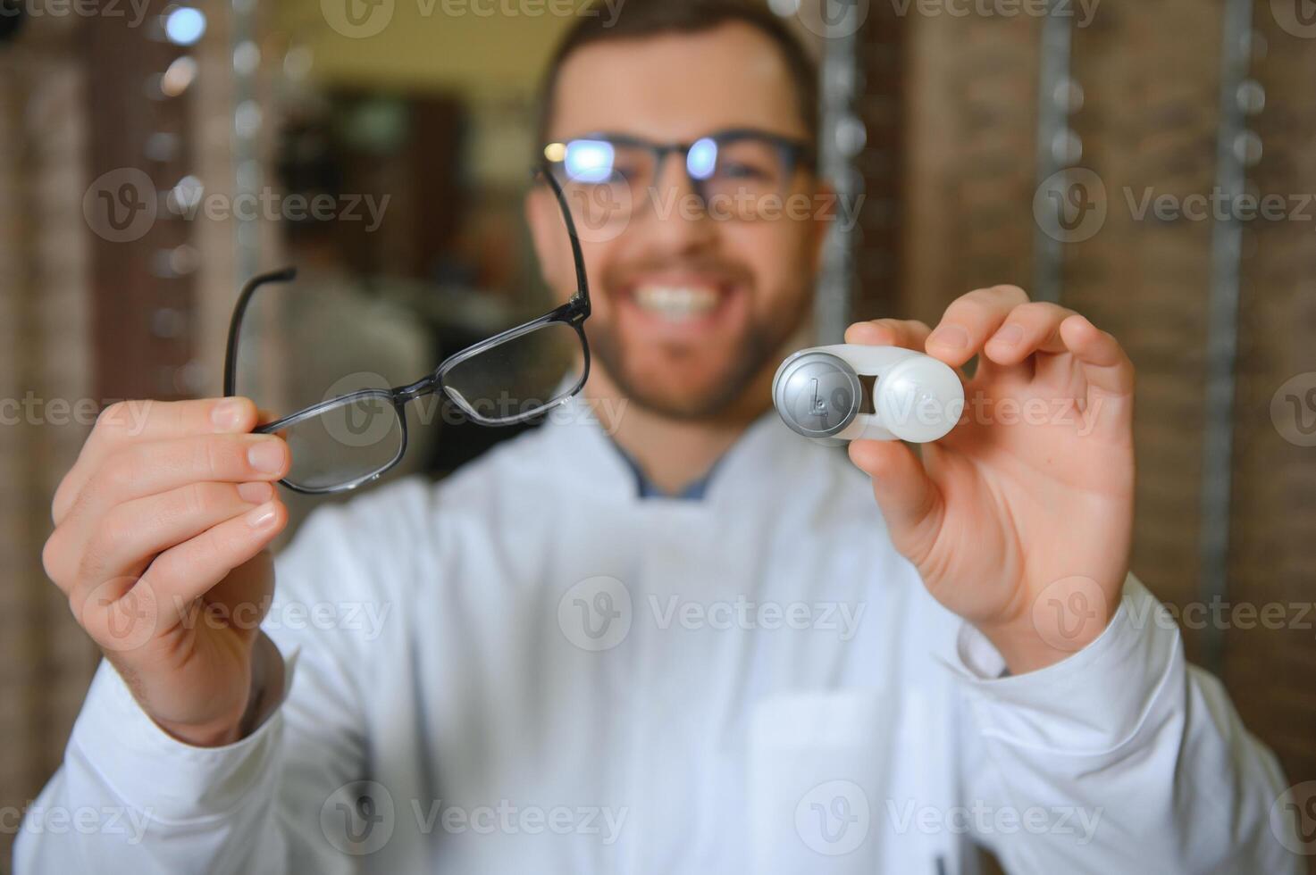 Male doctor holding contact lens case and glasses, indoors photo