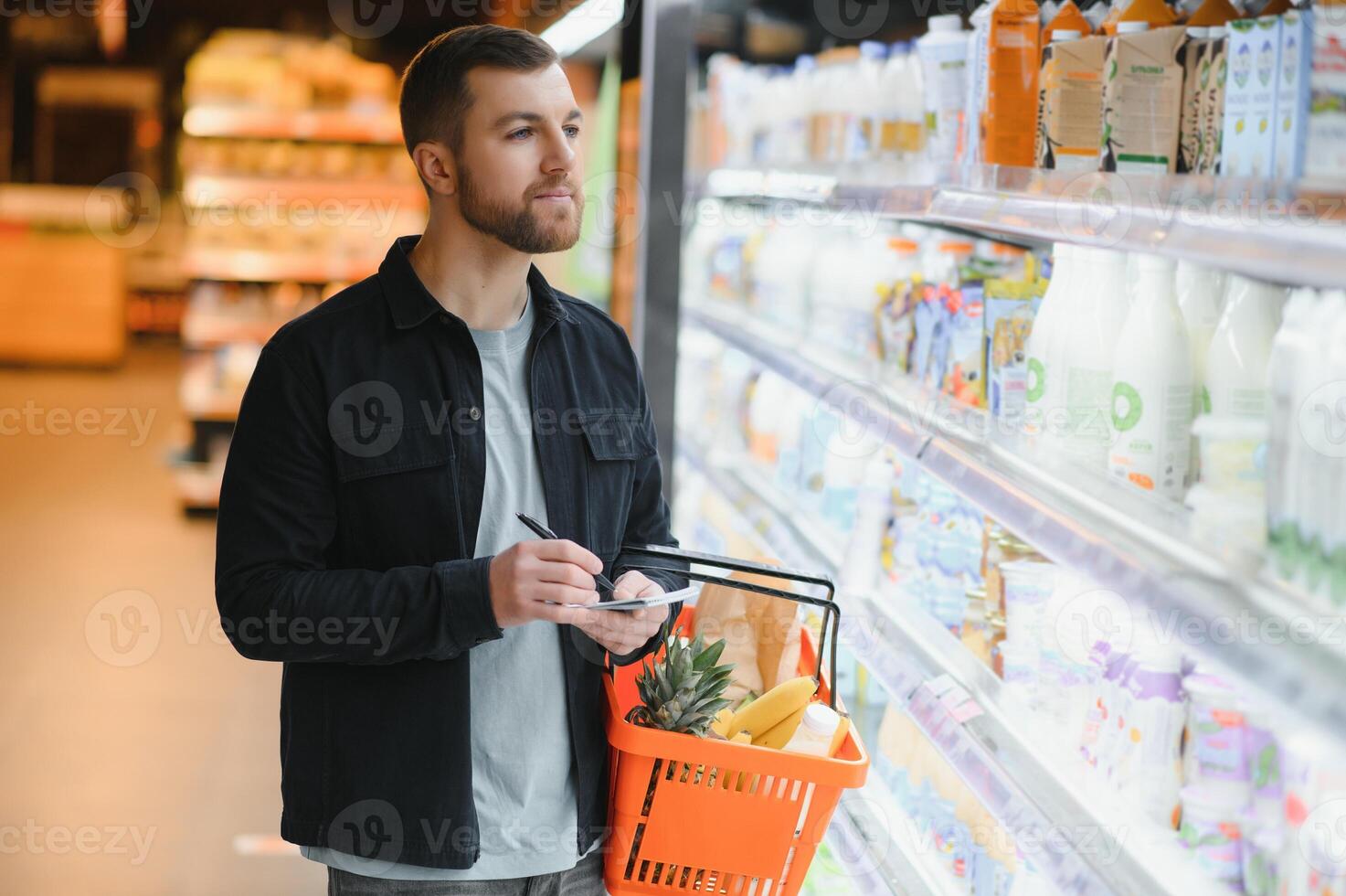 Young man buying groceries at the supermarket. Other customers in background. Consumerism concept. photo