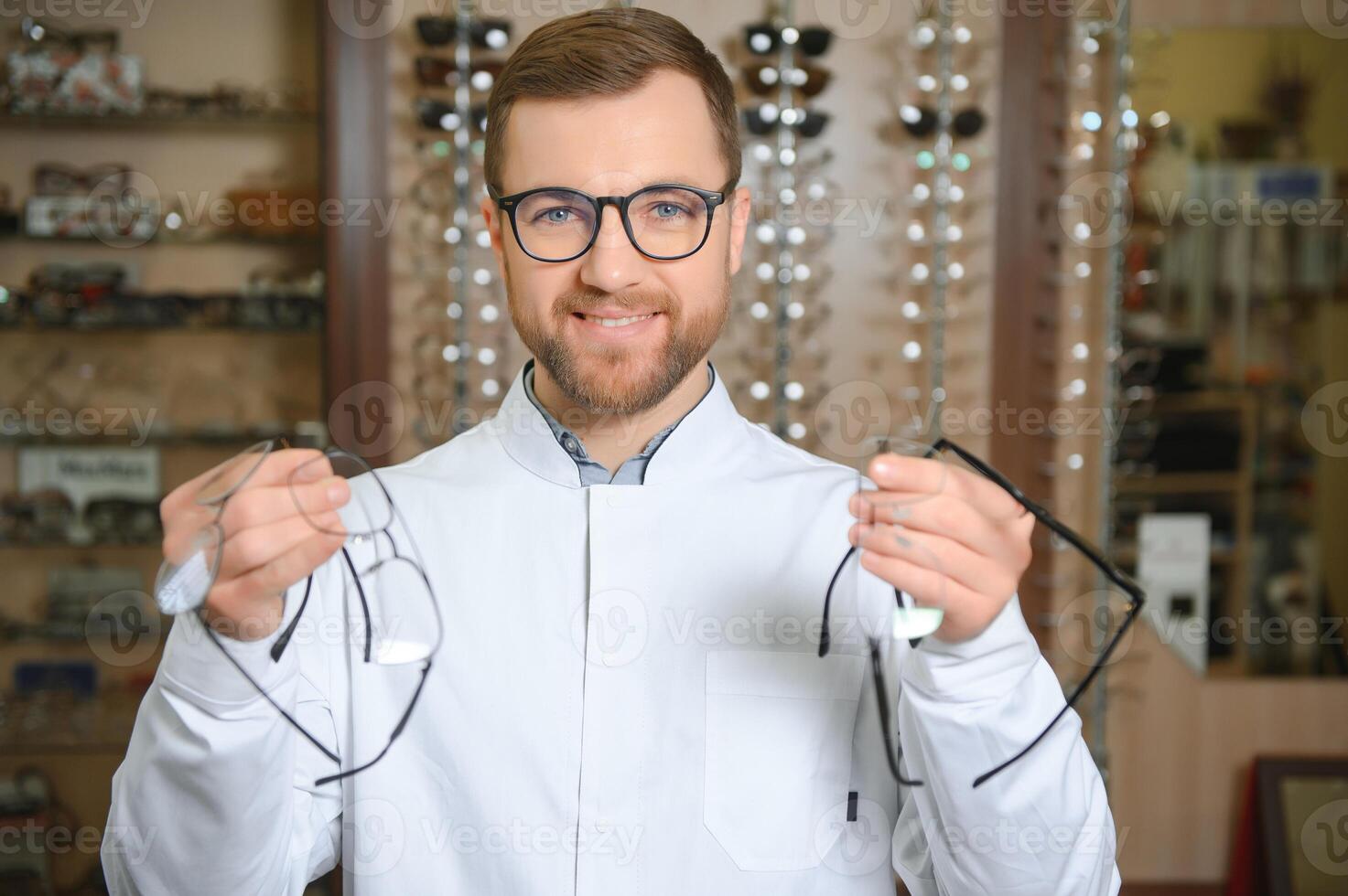 Handsome ophthalmologist holding eyeglasses for a try out. Optometrist offering to wear a pair of glasses. photo