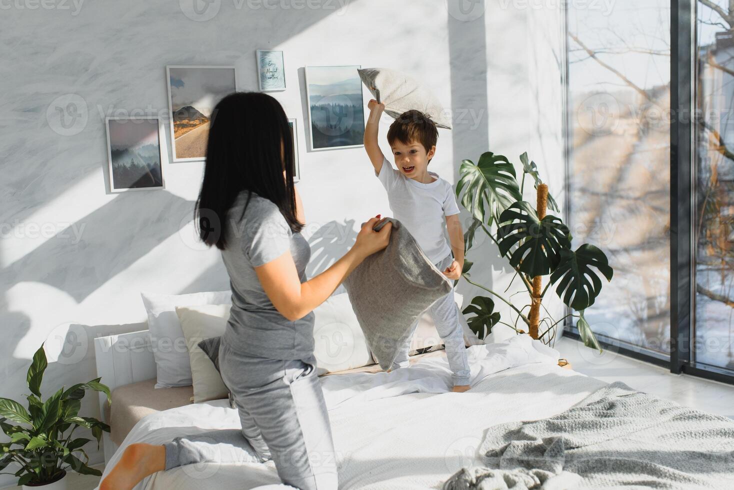 contento madre y hijo luchando con almohadas en cama en fin de semana Mañana foto