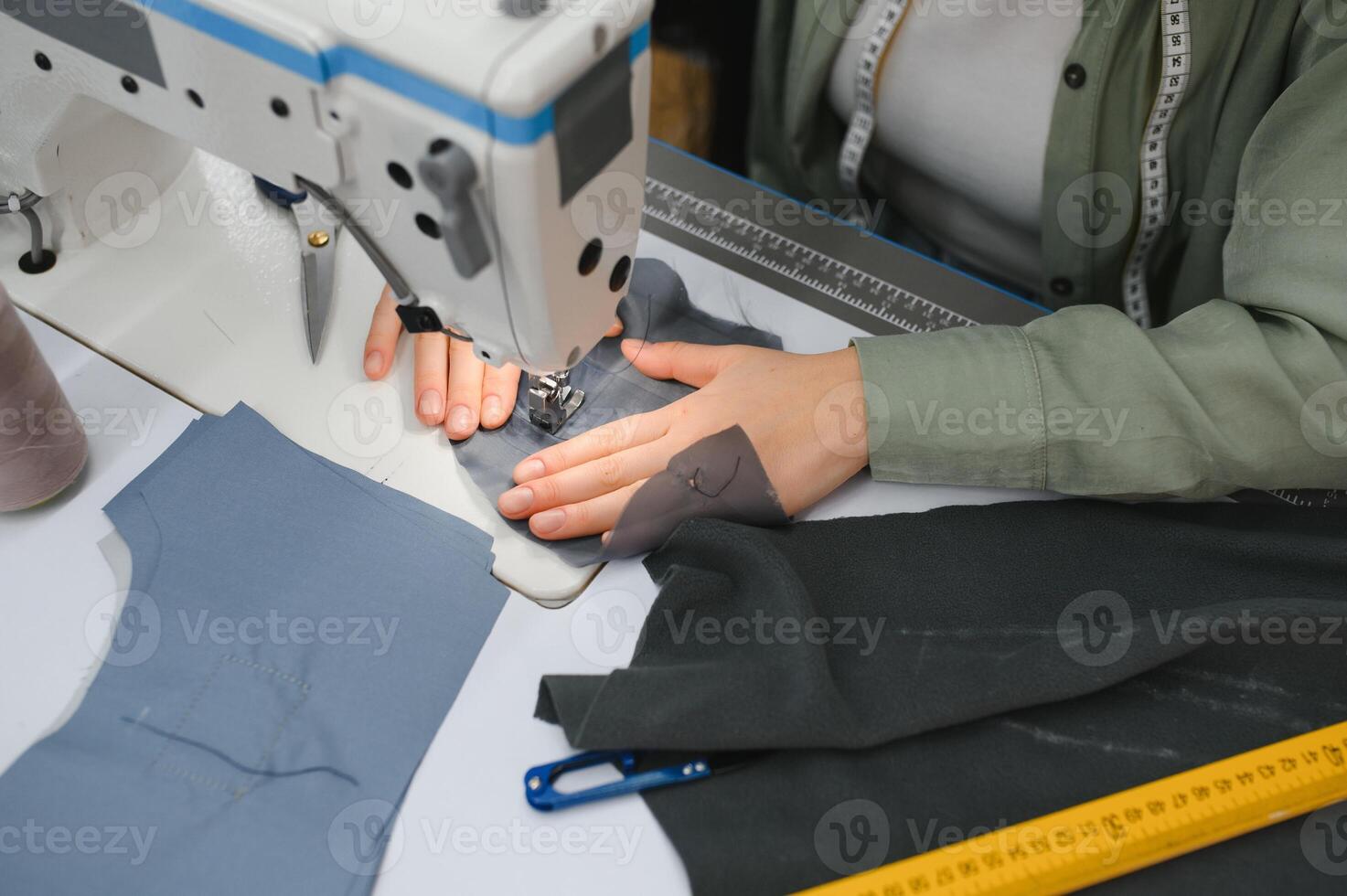 Young dressmaker woman sews clothes on working table. Smiling seamstress and her hand close up in workshop. photo