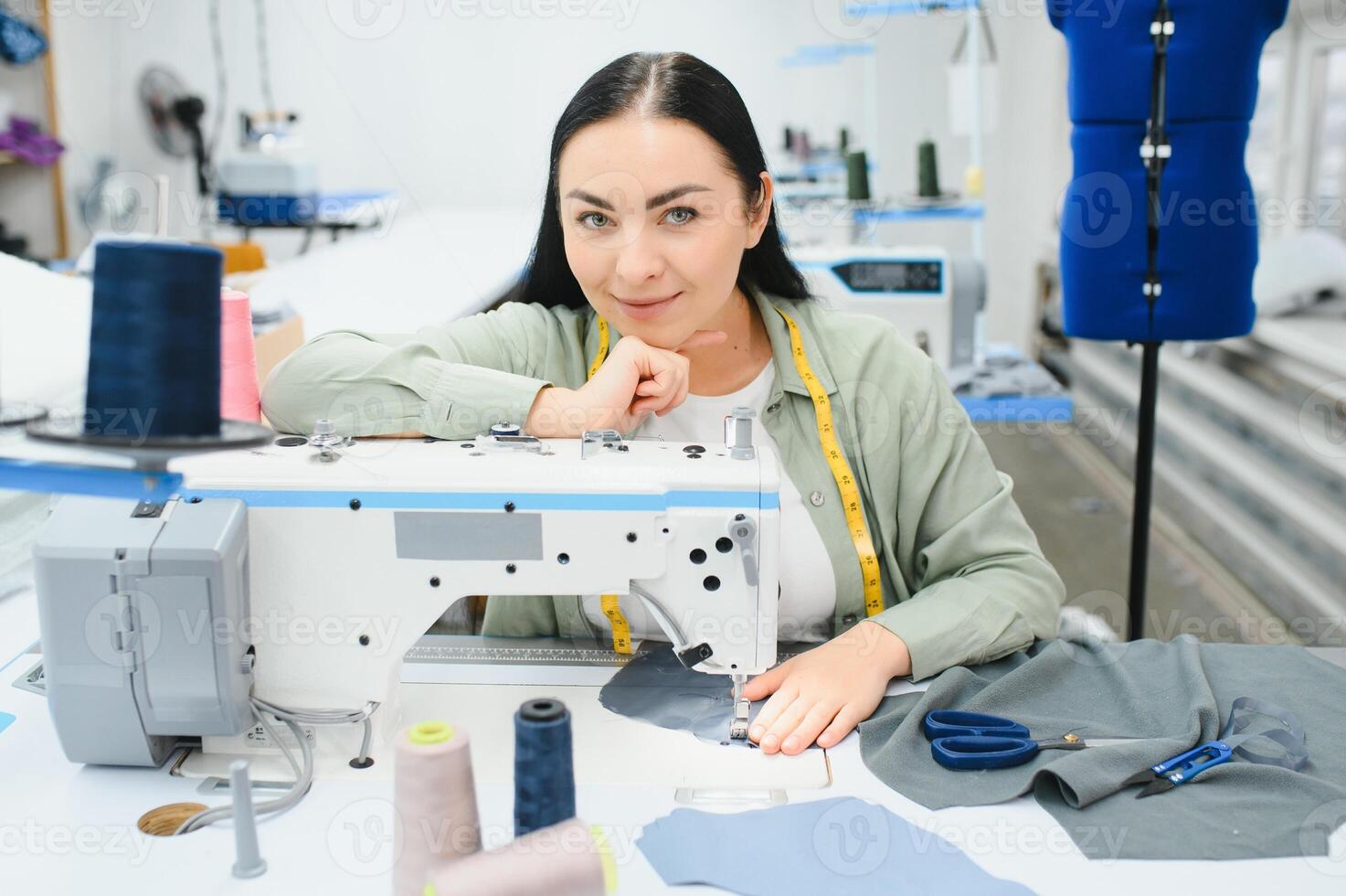 Positive young woman sewing with professional machine at workshop. photo