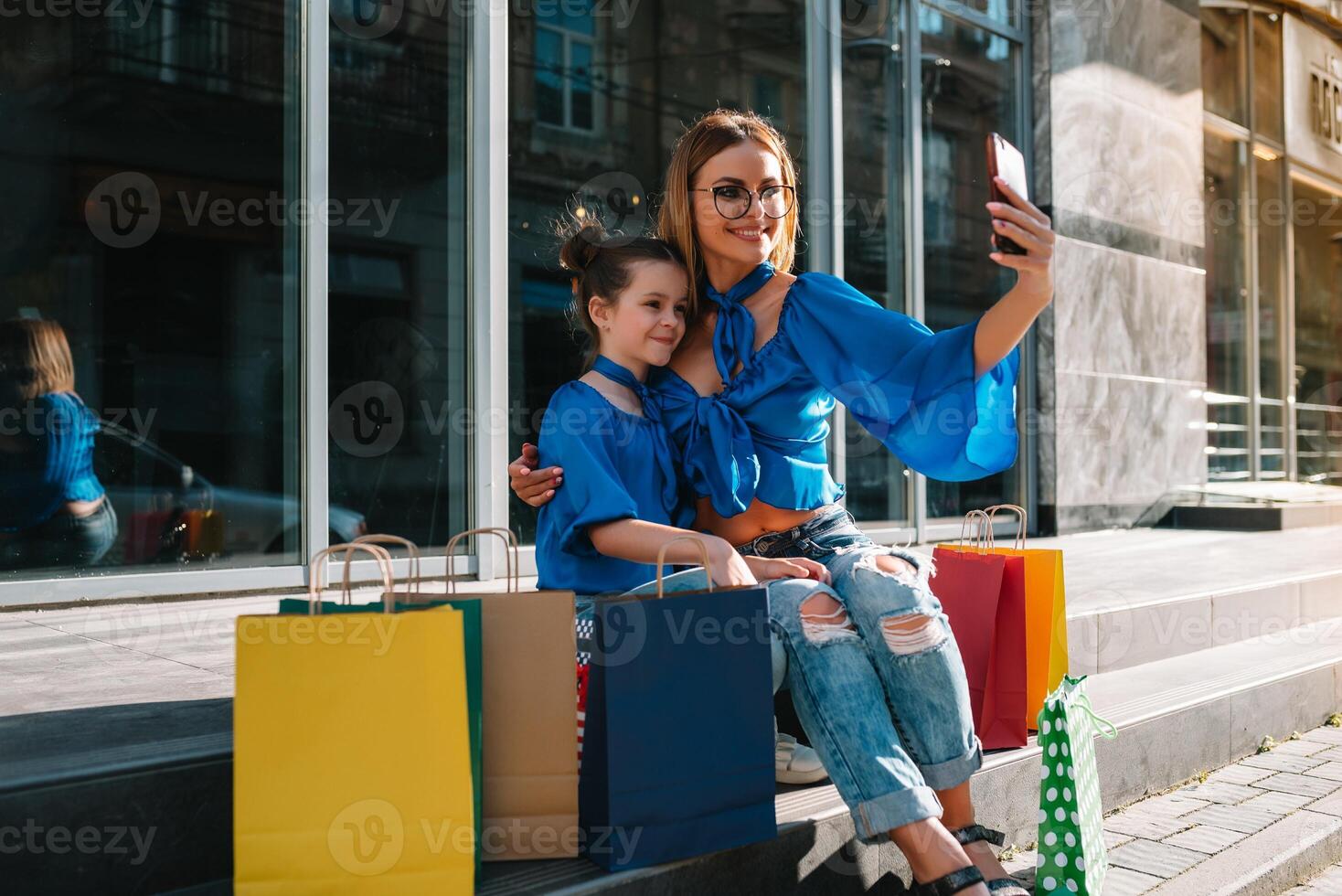 Young mother and her daughter doing shopping together. woman with girl child after shopping in street. woman with daughter with shopping bags outdoors. Woman and her daughter after shopping photo