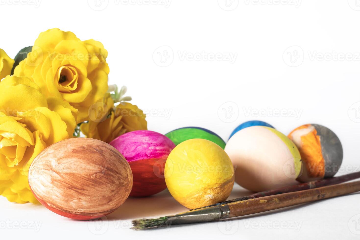 Colorful easter eggs with paint brushes and yellow flowers on a white background photo