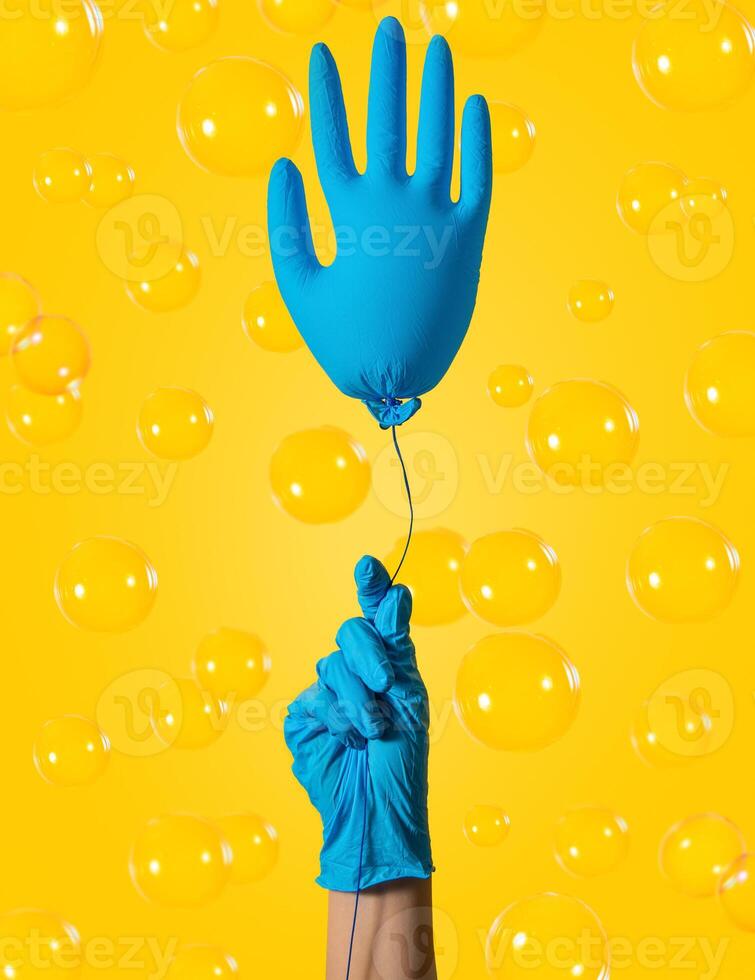 Cleaning concept. A hand in a blue glove holds a ball in the form of a glove on a yellow background. Spring cleaning. photo