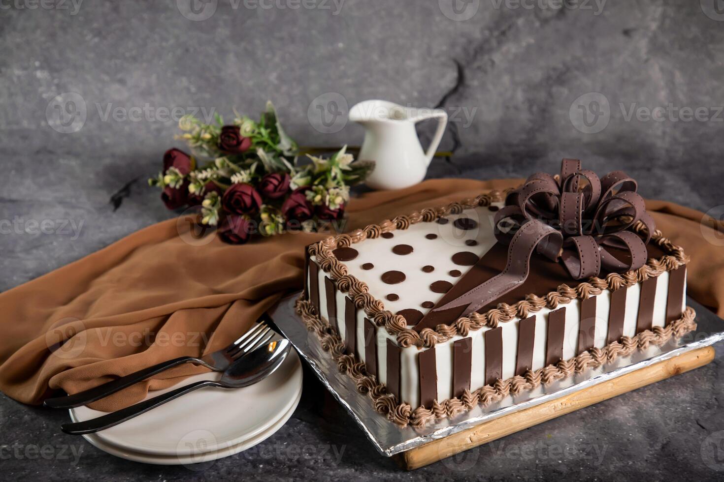 Square Chocolate Cake with rose flowers, spoon and fork served on board isolated on napkin side view of cafe baked food photo