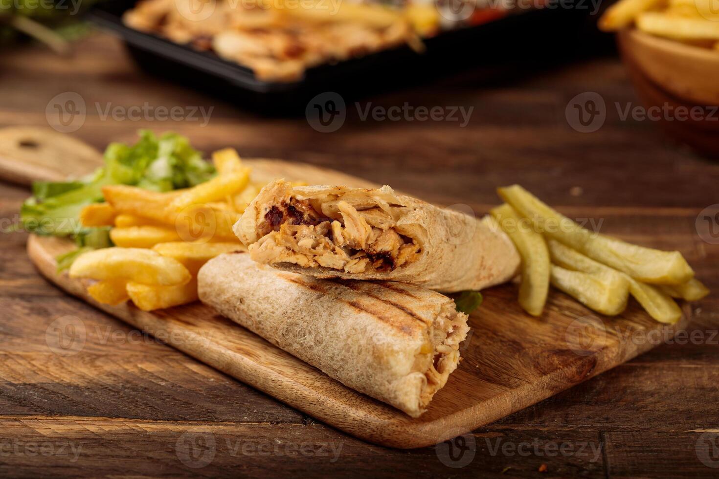 Chicken Wrap shawarma with fries served in a cutting board isolated on wooden table background side view of fastfood photo