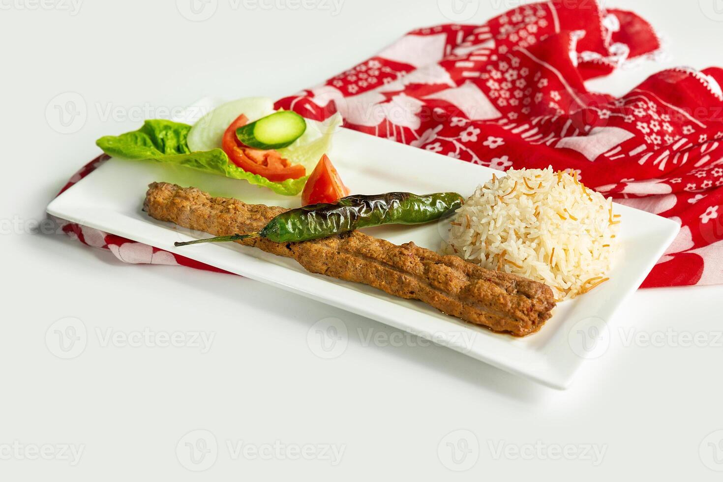 Turkish style adana kebab with rice and salad in a dish isolated on colorful table cloth side view on grey background photo