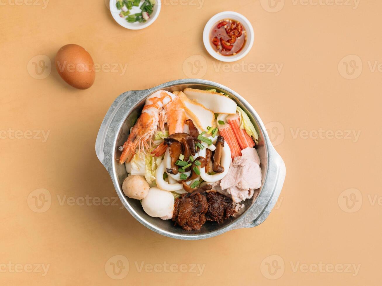 Tom Yum Xiao Wan in a bowl with soup, chili sauce and spring onion top view on wooden table photo