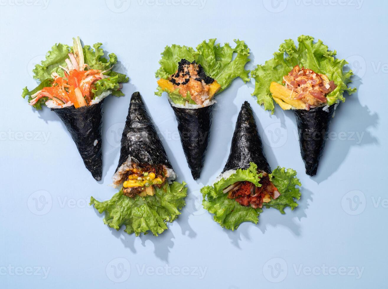 Assorted japanese wraps Spicy TAMAGO, CALIFORNIA wrap, POKE SALMON Skin, SPICY TUNA roll topping with salad leaves isolated on sky blue background top view fast food photo