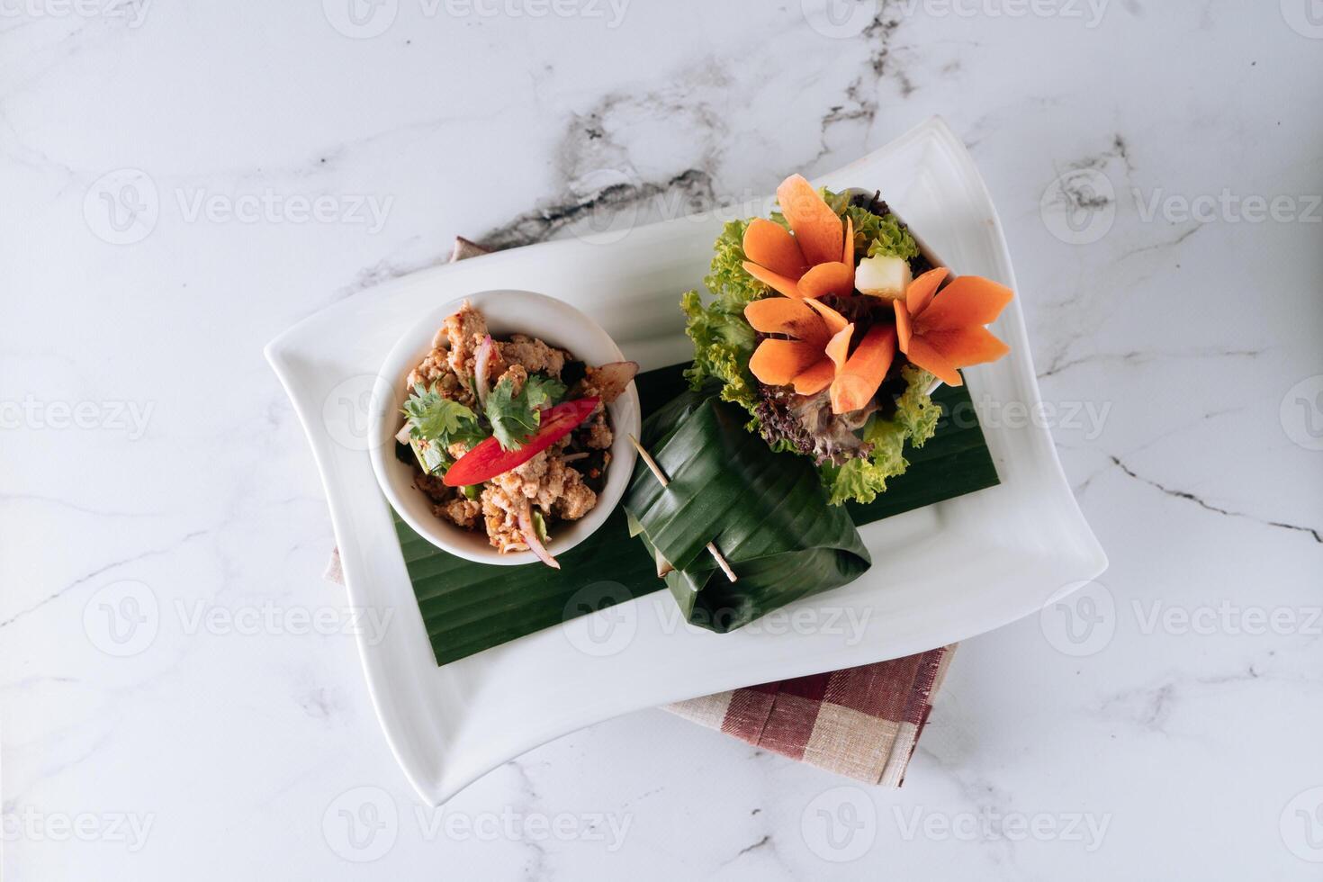Spicy fried Larb Chicken with salad leaf in a dish isolated on mat top view on grey marble background photo