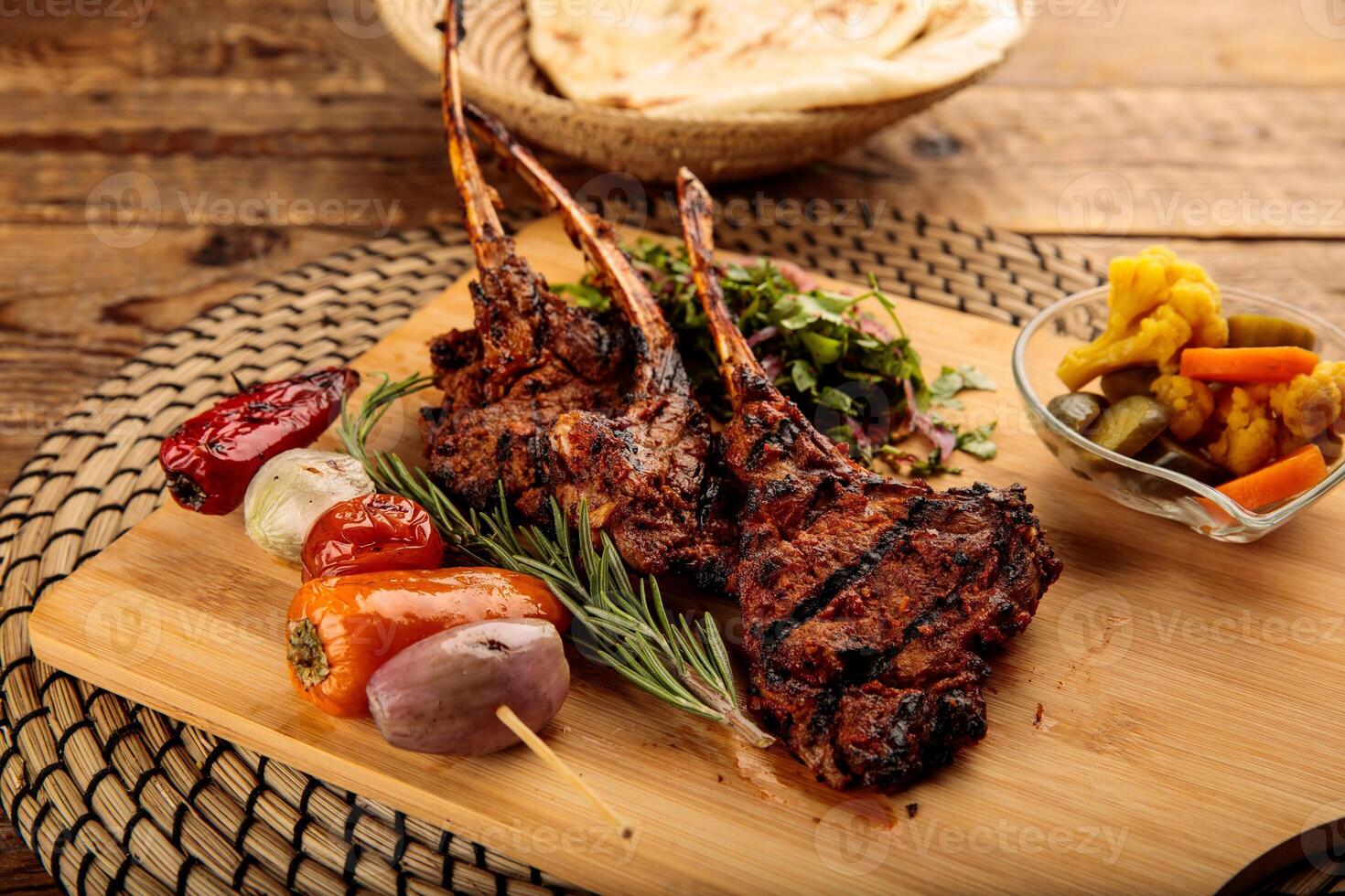 Lamb Chops with pickle and bread served in a wooden cutting board isolated on wooden background side view photo