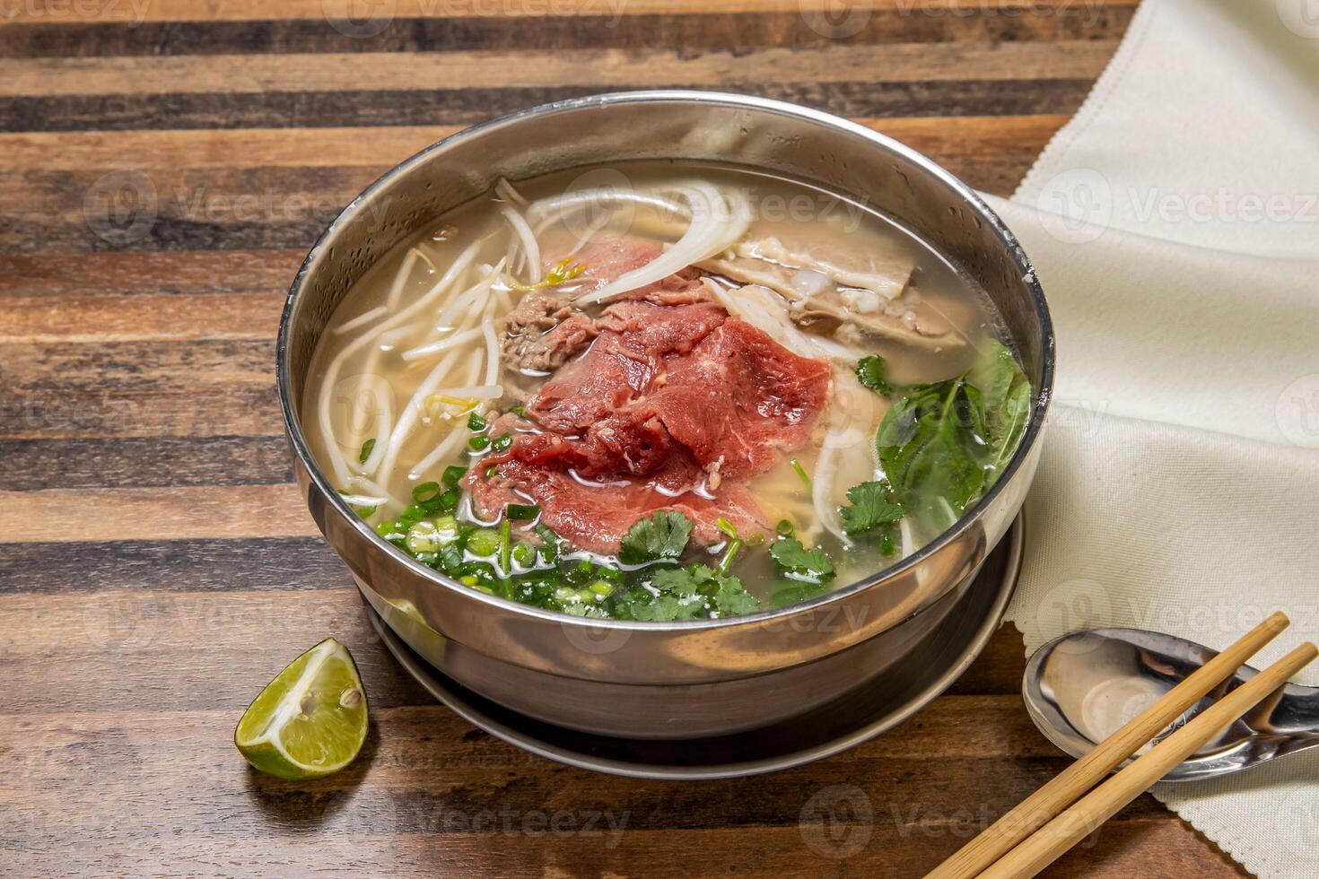 Hanoi rare Beef Pho topping with onion, noodles, green onion, lemon and coriander served in bowl isolated on wooden table top view of hong kong fast food photo