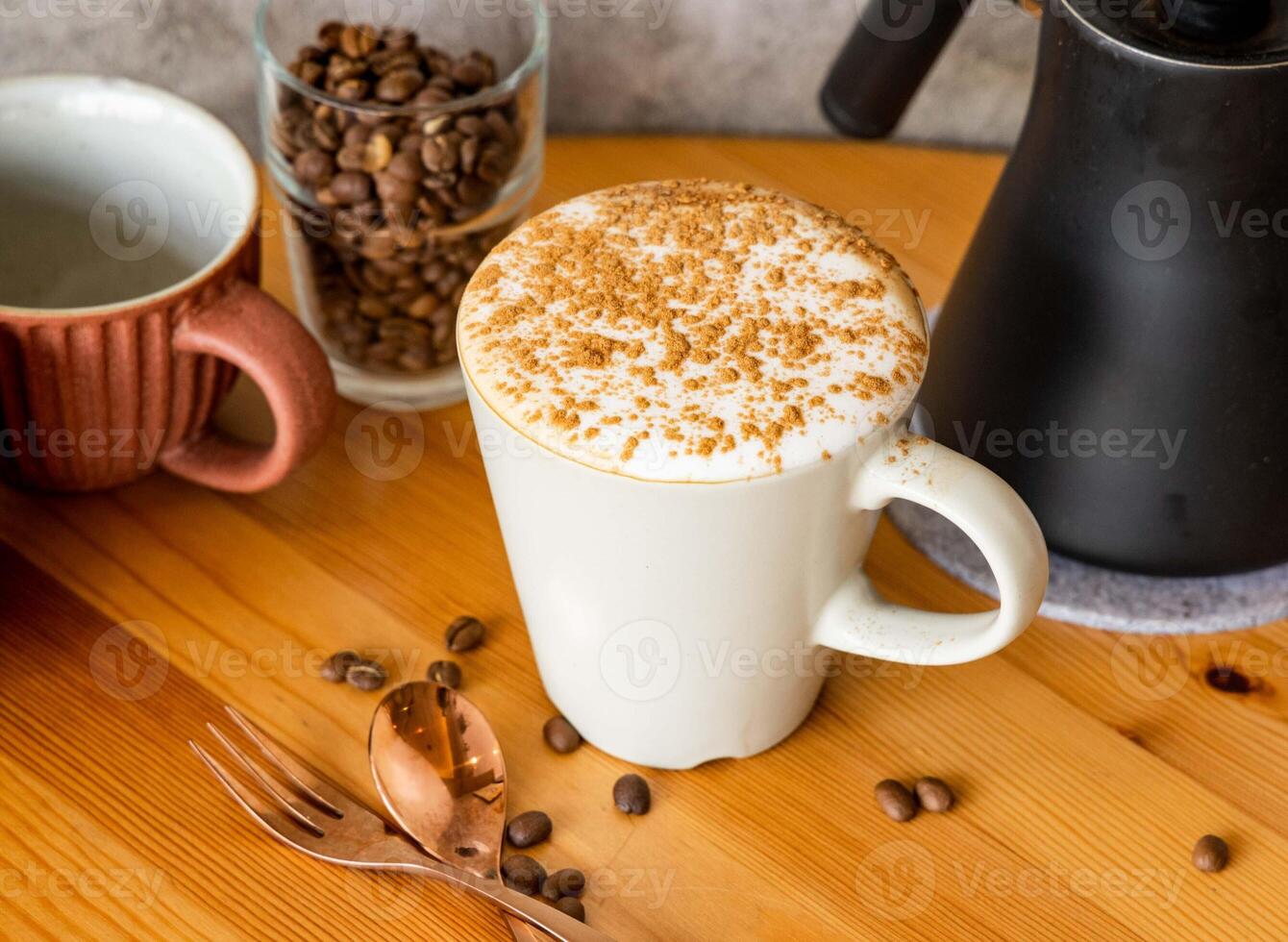 Cappuccino with cinnamon powder, coffee beans, fork, spoon served in cup isolated on wooden table top view of taiwan food photo