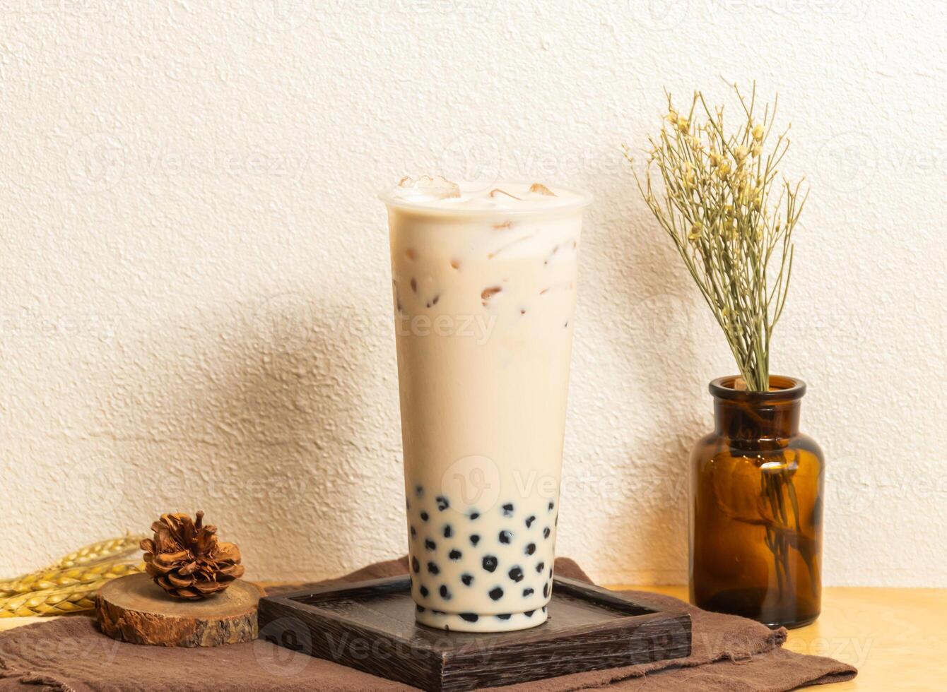 Iced Pearl milk tea served in disposable glass isolated on wooden board side view of taiwanese ice drink photo