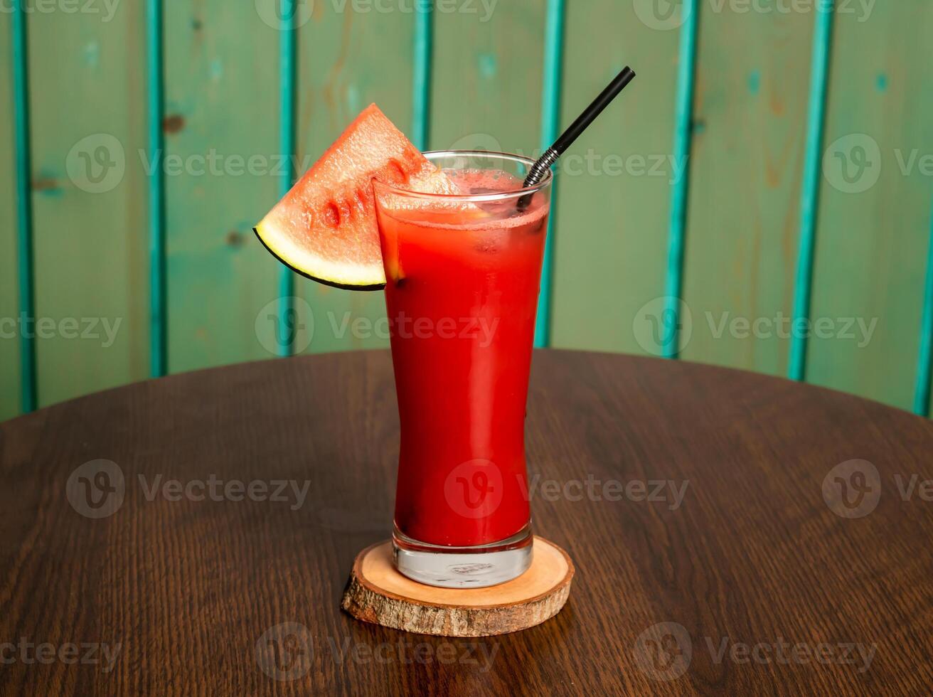 A glass of watermelon juice shake with raw watermelon, straw isolated on wooden table side view healthy drink for vitamin c photo