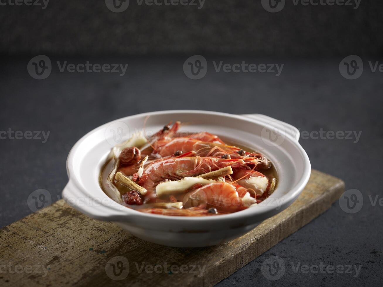 Poached Tiger Prawns with Superior Stock and Chinese Herbs served in a pot isolated on cutting board side view on dark background photo