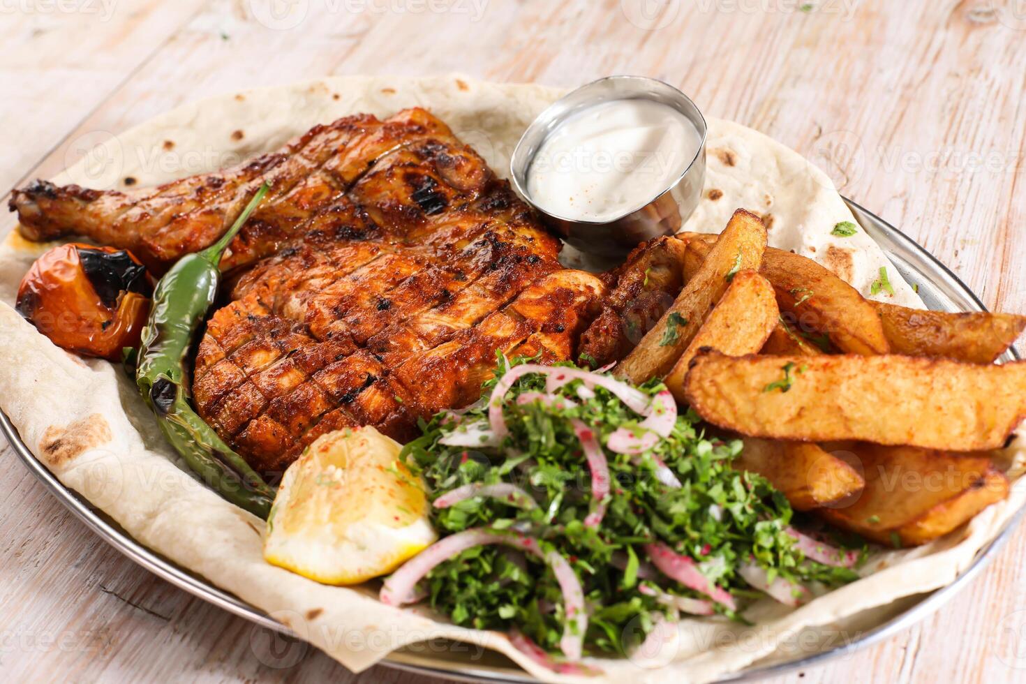 Half grilled chicken with salad, wedges, lemon and dip served in dish isolated on background top view of arabic food photo