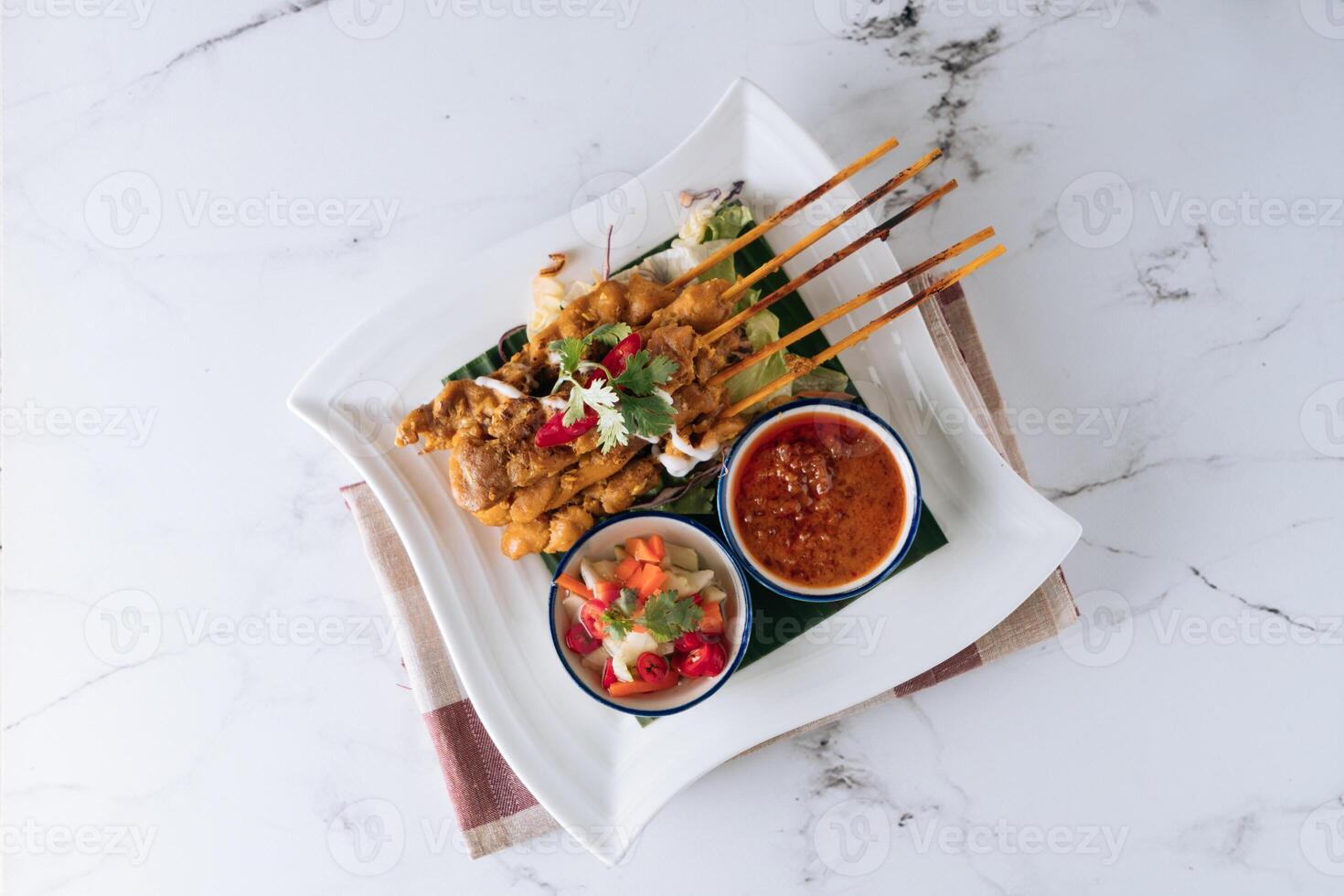 Traditional Malaysian food chicken satay skewers with chili sauce and salad in a dish isolated on mat top view on grey marble background photo