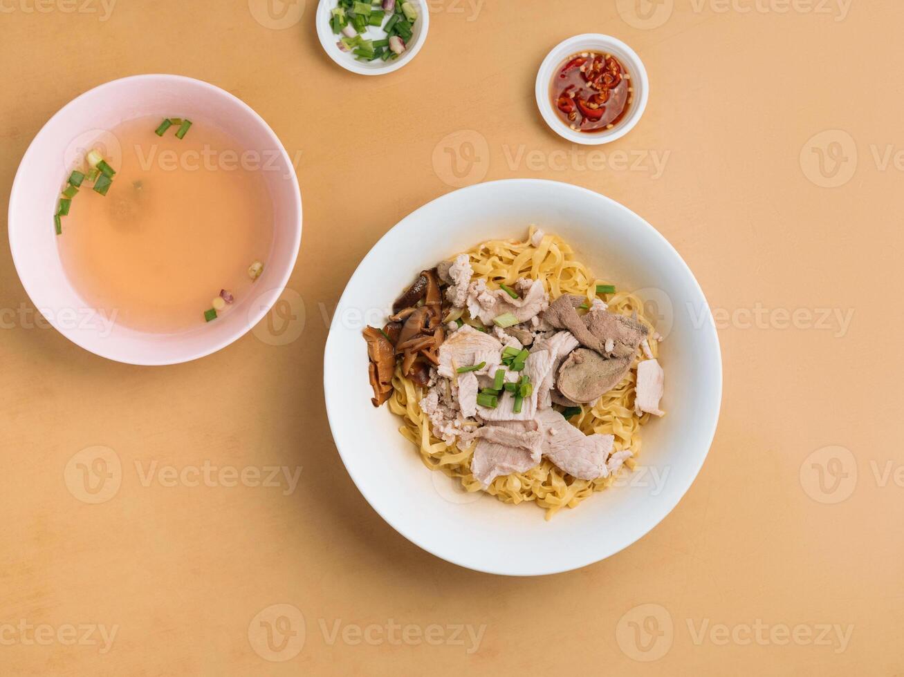 Minced meat Noodle in a bowl with soup, chili sauce and spring onion top view on wooden table photo