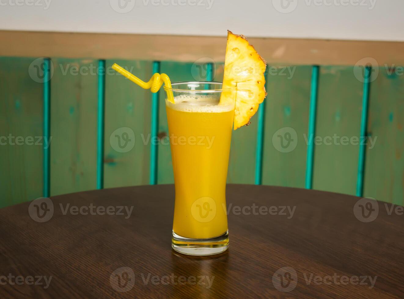 A glass of healthy pineapple juice with straw isolated on dark wooden table side view photo