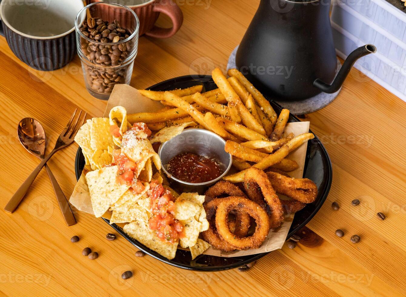 meriendas plato con francés papas fritas, frito cebolla anillos, nachos, chile salsa, café frijoles, tenedor, cuchara servido en plato aislado en de madera mesa parte superior ver de Taiwán comida foto