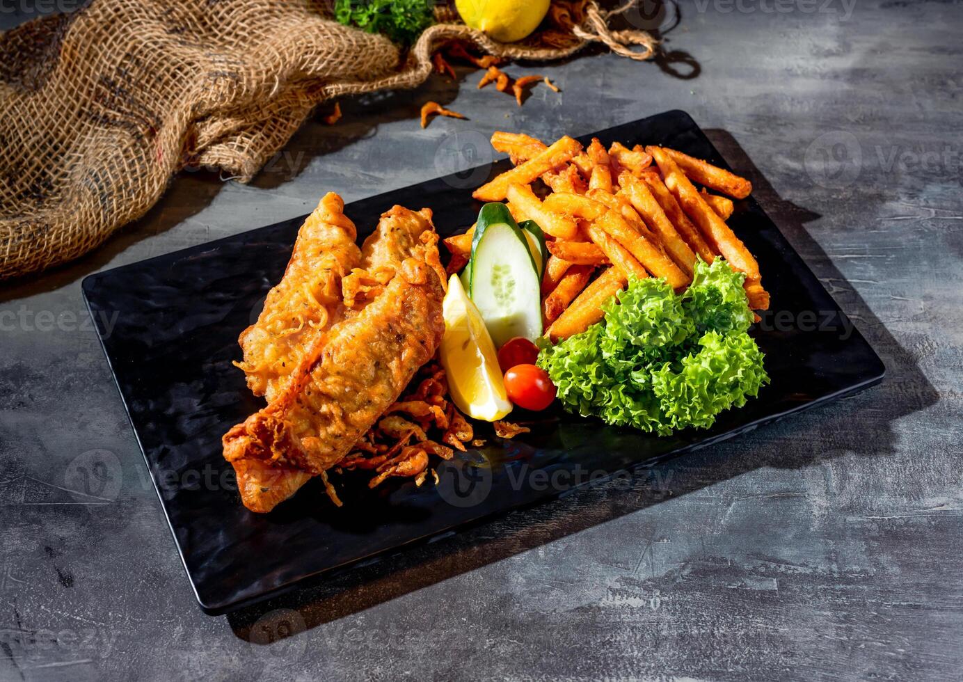 Fried Red Tilapia fish with salad, lime and fries in a dish side view on dark background photo