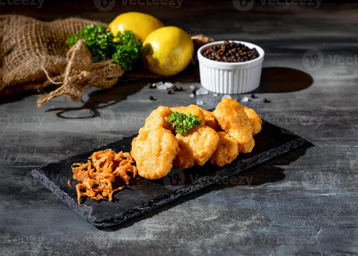 Chicken Nuggets on wooden board with black pepper and lime top view on dark background photo