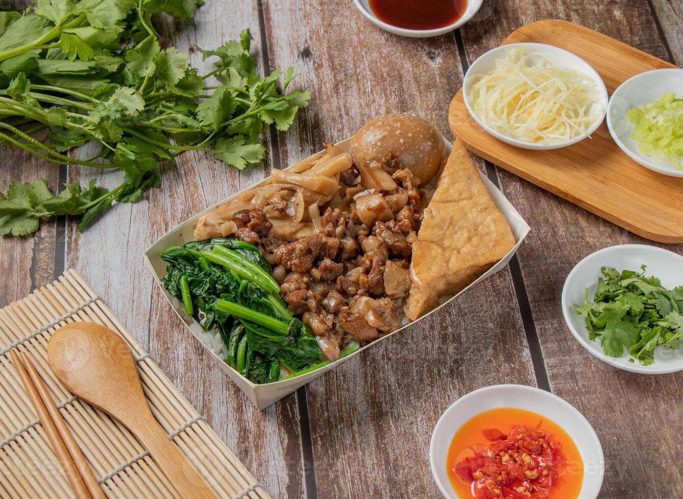 Dried Pork meat bento include Pig feet, rice, braised pork, with chilli sauce, noodles, bread, toast, spoon and chopsticks served in dish isolated on napkin top view of hong kong food photo