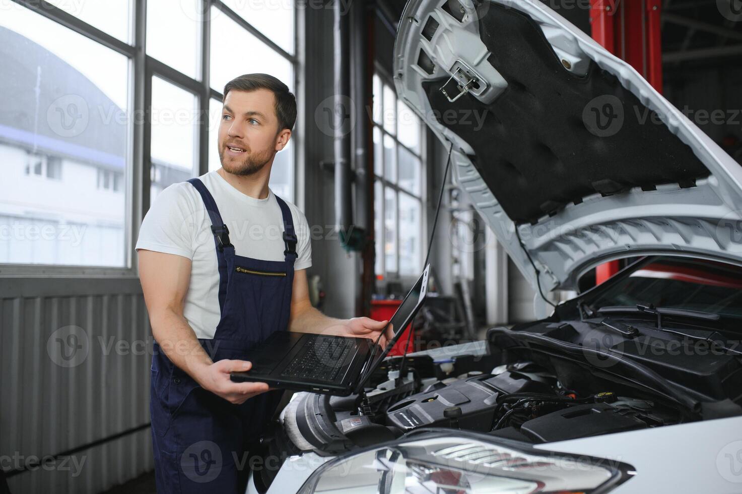 mecánico hombre mecánico gerente trabajador utilizando un ordenador portátil computadora comprobación coche en taller a auto coche reparar Servicio centro. ingeniero joven hombre mirando a inspección vehículo detalles debajo coche capucha foto