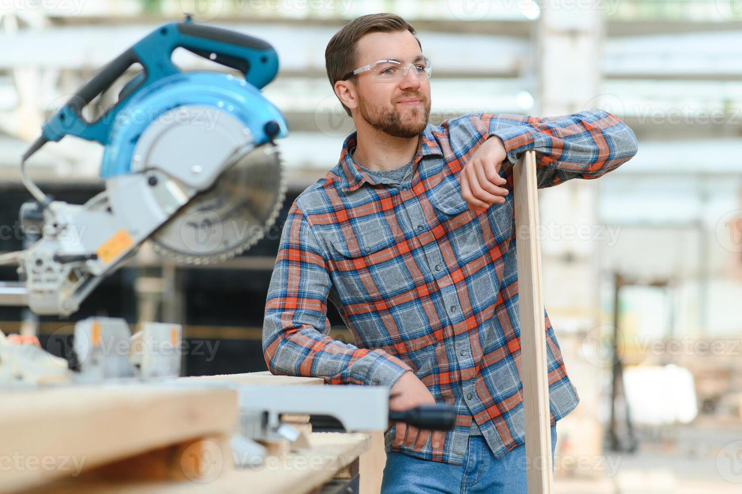 A carpenter works on woodworking the machine tool. Man collects furniture boxes. Saws furniture details with a circular saw. Process of sawing parts in parts. Against the background of the workshop. photo