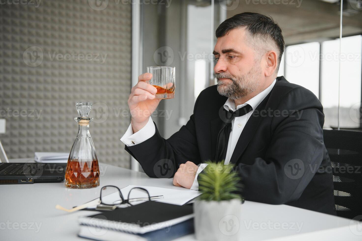 Old male employee drinking alcohol at workplace photo