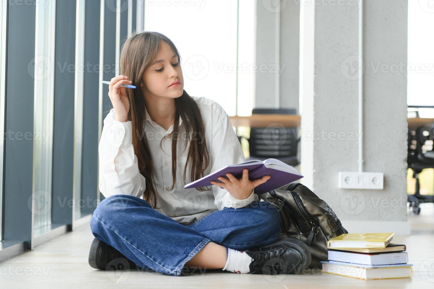 Girl smiling. Beautiful schoolgirl smiling while sitting near window and reading book photo