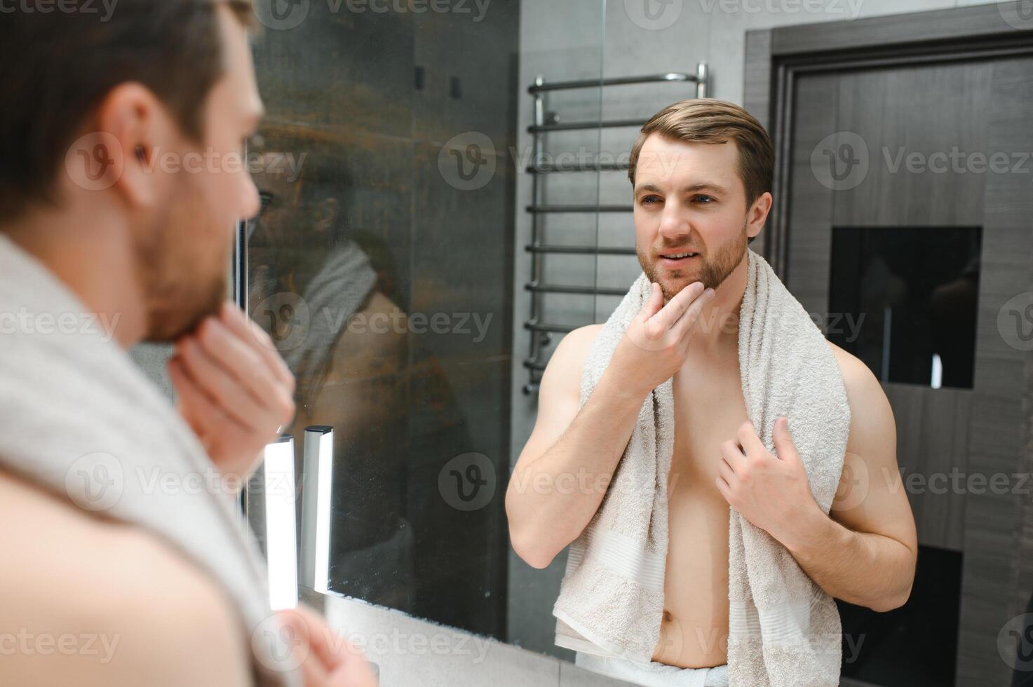 Young man looking in mirror after shaving at home photo