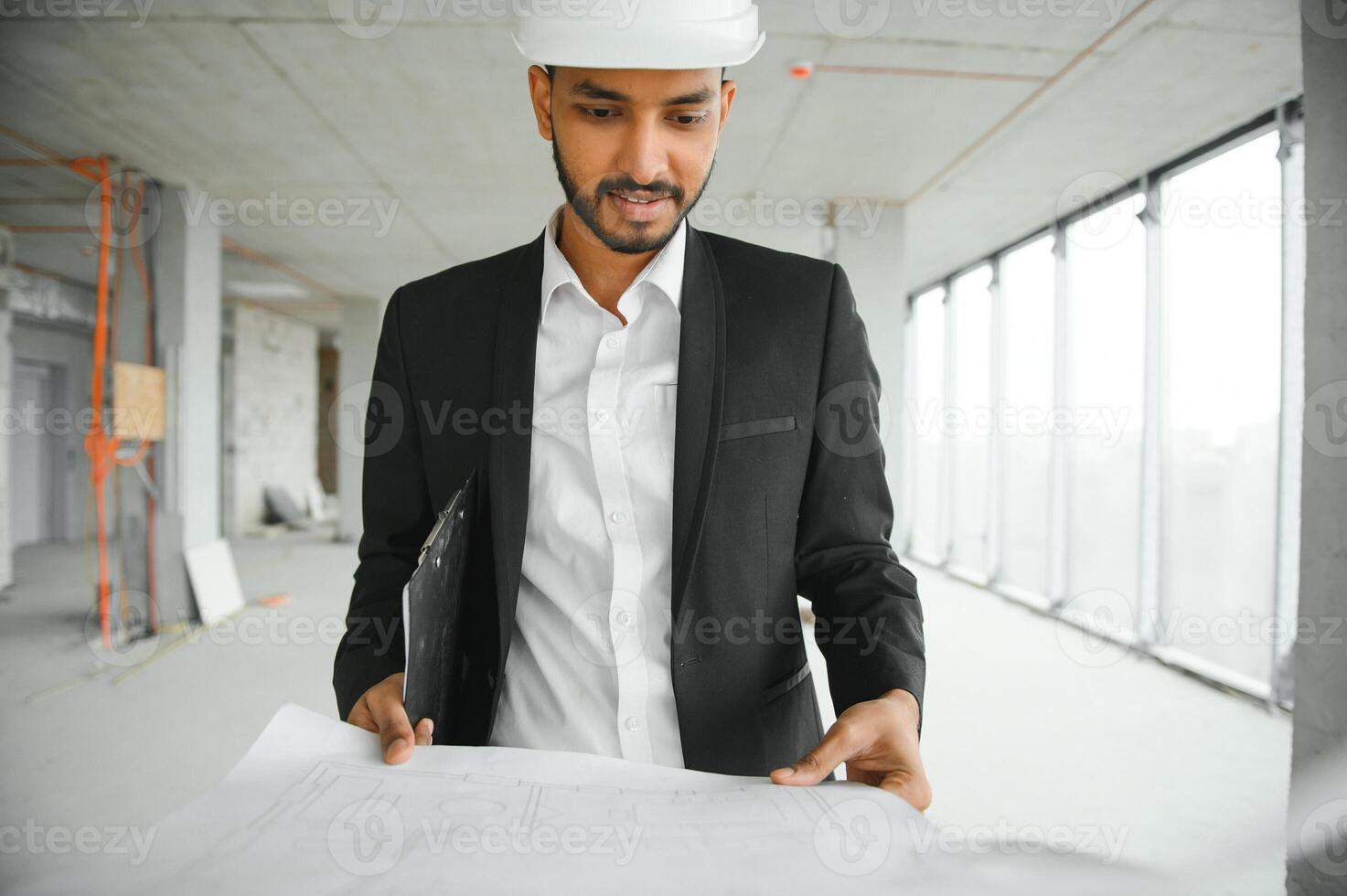 Indian construction site manager standing wearing helmet, thinking at construction site. Portrait of mixed race manual worker or architect. photo